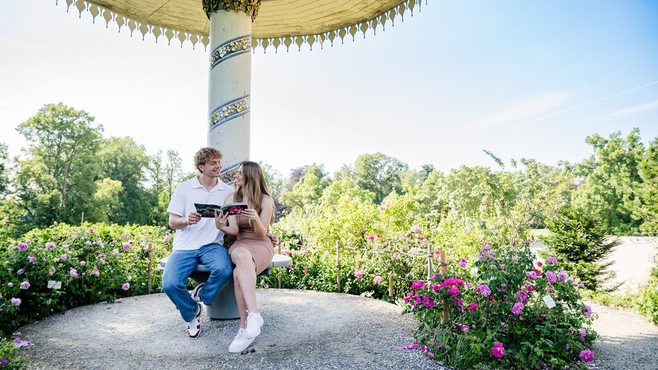 Paar sitzt im Schlosspark von Schloss Eggenberg und schaut in ein Buch. | © Graz Tourismus - Mias Photoart